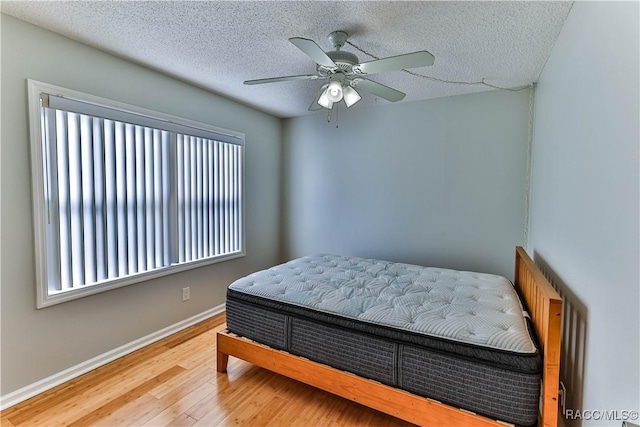 bedroom with ceiling fan, baseboards, a textured ceiling, and wood finished floors