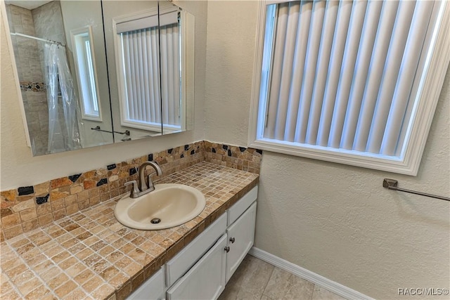 bathroom with curtained shower, decorative backsplash, baseboards, vanity, and a textured wall