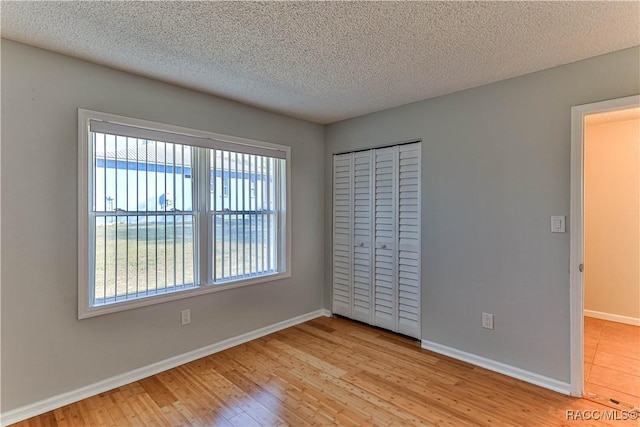 unfurnished bedroom featuring a closet, baseboards, a textured ceiling, and wood finished floors