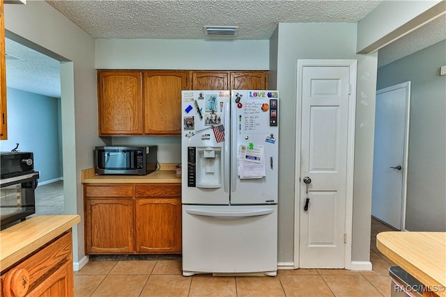 kitchen with light countertops, light tile patterned floors, brown cabinetry, and white fridge with ice dispenser