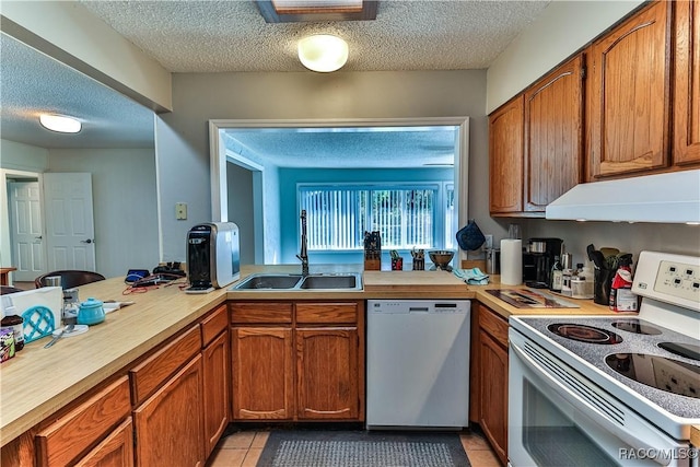 kitchen featuring under cabinet range hood, light tile patterned floors, brown cabinetry, white appliances, and a sink