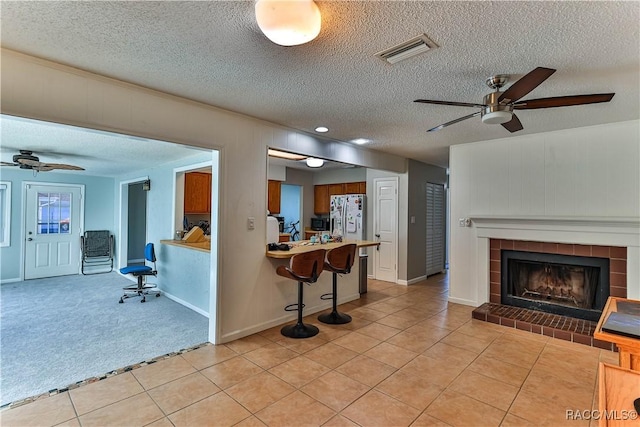 living area featuring light tile patterned floors, visible vents, ceiling fan, a textured ceiling, and light colored carpet