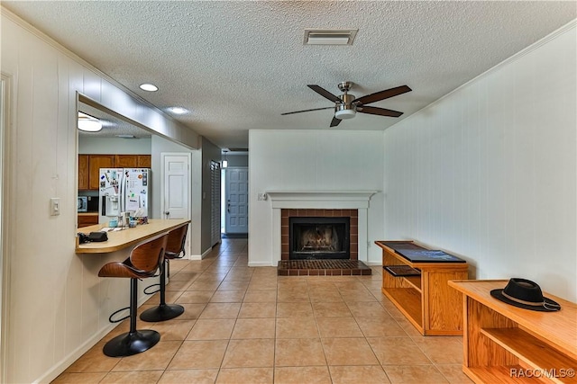 living room featuring a ceiling fan, visible vents, light tile patterned flooring, a fireplace, and a textured ceiling