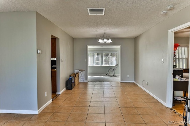 unfurnished dining area featuring light tile patterned floors, baseboards, visible vents, a textured ceiling, and a notable chandelier