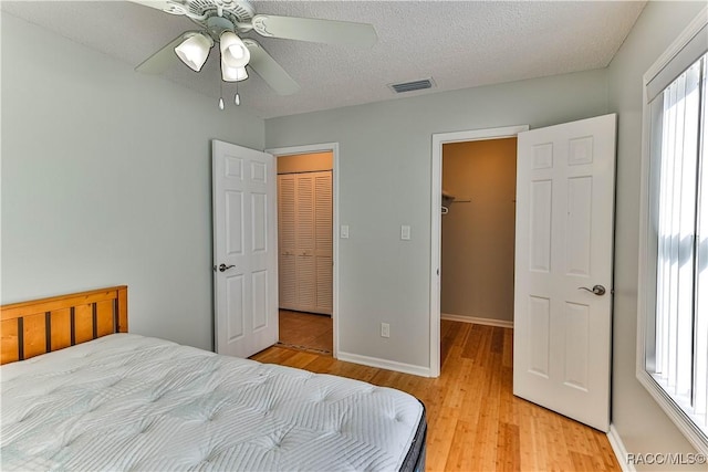 bedroom featuring baseboards, visible vents, light wood finished floors, a textured ceiling, and a walk in closet