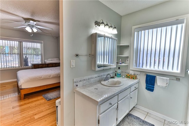 bathroom featuring wood finished floors, a ceiling fan, baseboards, and a textured ceiling