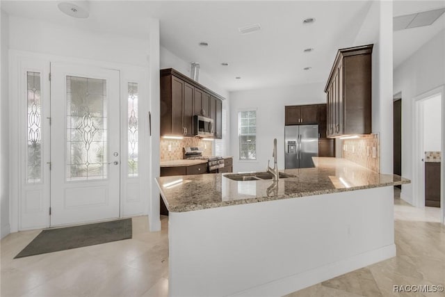 kitchen with light stone countertops, sink, kitchen peninsula, backsplash, and stainless steel appliances