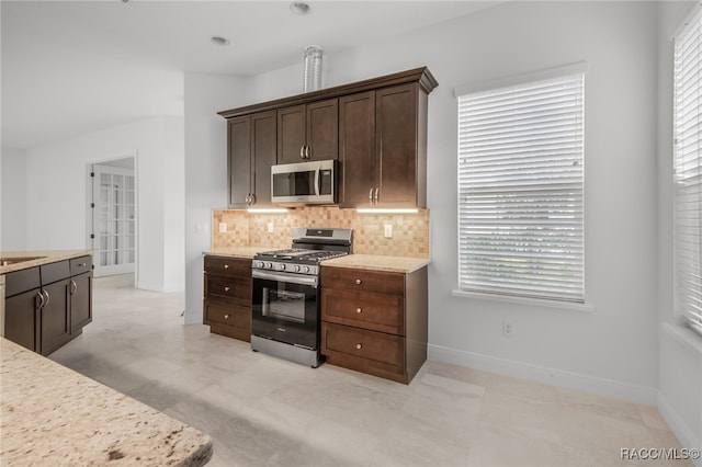 kitchen with dark brown cabinets, light stone counters, decorative backsplash, and appliances with stainless steel finishes