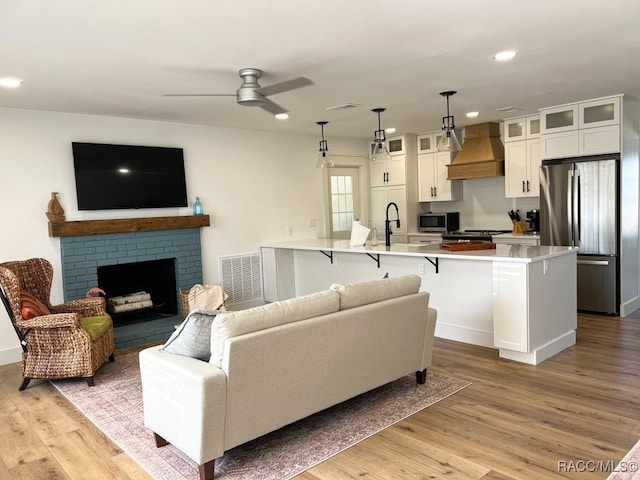 living room with light wood-type flooring, a brick fireplace, and visible vents