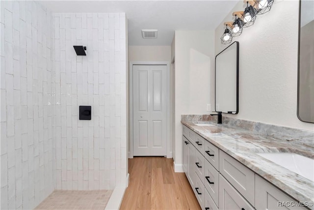 bathroom with wood-type flooring, tiled shower, and vanity