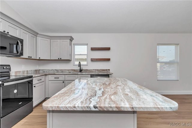 kitchen with sink, appliances with stainless steel finishes, gray cabinetry, a kitchen island, and light wood-type flooring