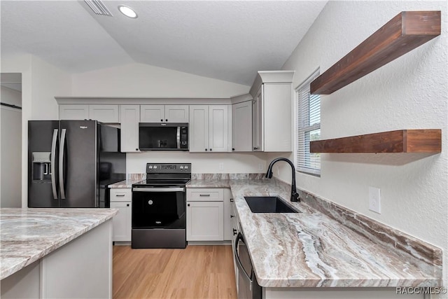 kitchen featuring lofted ceiling, sink, range with electric cooktop, light stone countertops, and black fridge