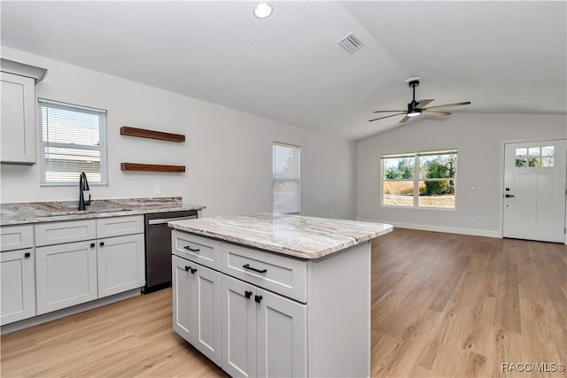 kitchen featuring sink, light stone counters, light wood-type flooring, dishwasher, and a kitchen island