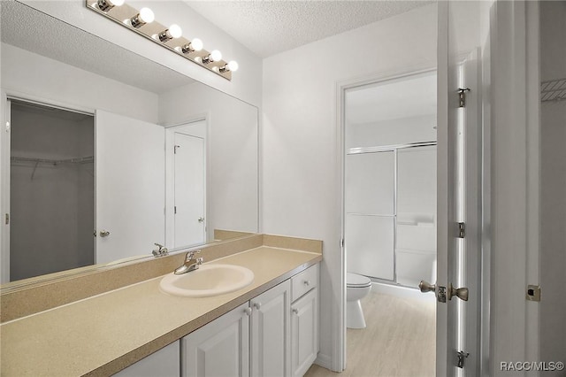 bathroom with vanity, a shower with shower door, toilet, a textured ceiling, and wood-type flooring