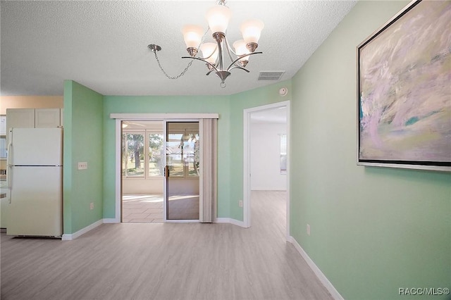 unfurnished dining area with a chandelier, a textured ceiling, and light hardwood / wood-style floors