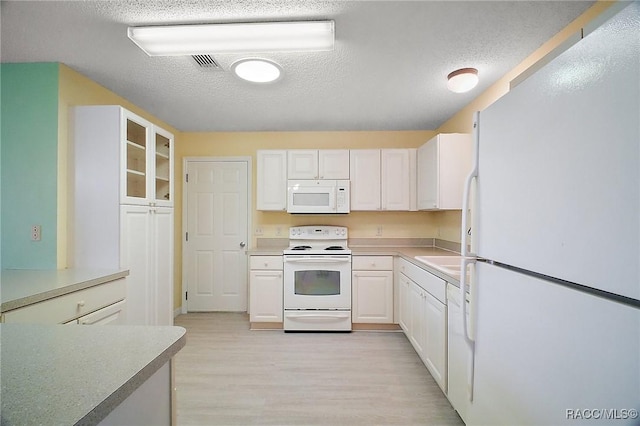 kitchen with light wood-type flooring, a textured ceiling, white appliances, and white cabinetry