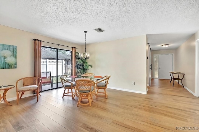 dining area with an inviting chandelier, light hardwood / wood-style floors, and a textured ceiling