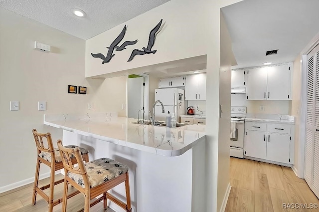 kitchen with white cabinetry, sink, a kitchen breakfast bar, kitchen peninsula, and white appliances