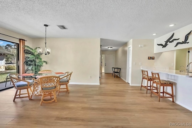 dining space featuring a notable chandelier, light hardwood / wood-style floors, sink, and a textured ceiling