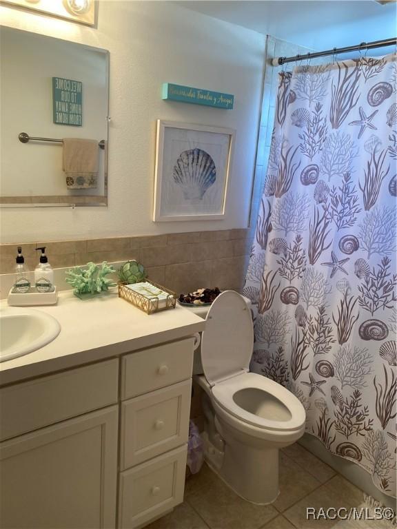 bathroom with a wainscoted wall, tile walls, toilet, vanity, and tile patterned flooring