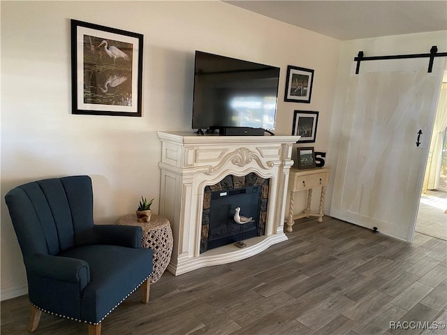 sitting room with dark wood-style floors, a fireplace with raised hearth, and a barn door