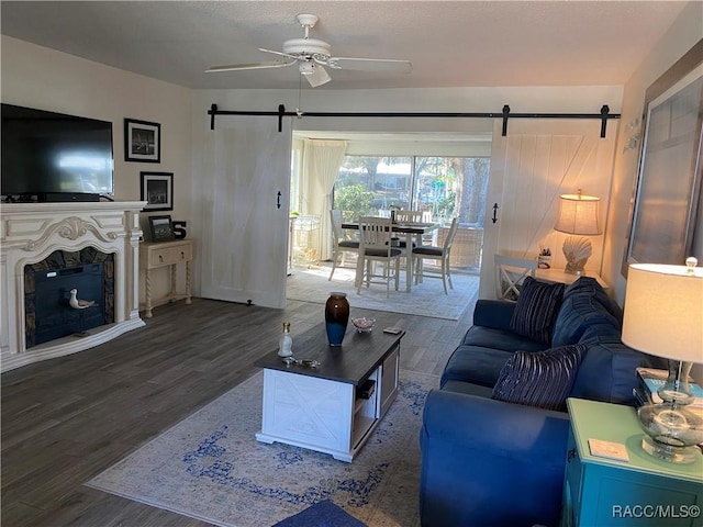 living area featuring ceiling fan, a fireplace, dark wood finished floors, and a barn door