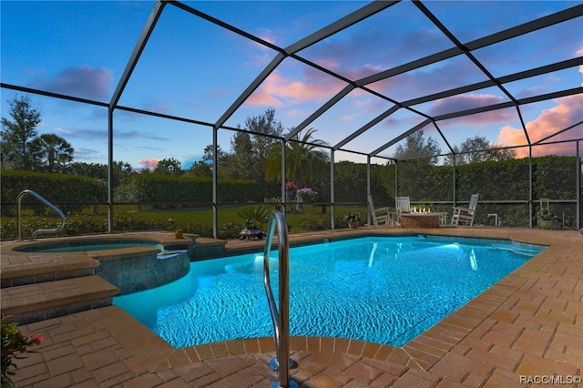 pool at dusk featuring a lanai, a patio area, and an in ground hot tub