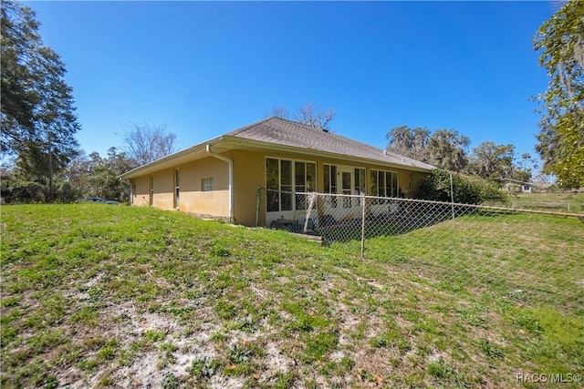 back of house featuring a lawn, stucco siding, and fence