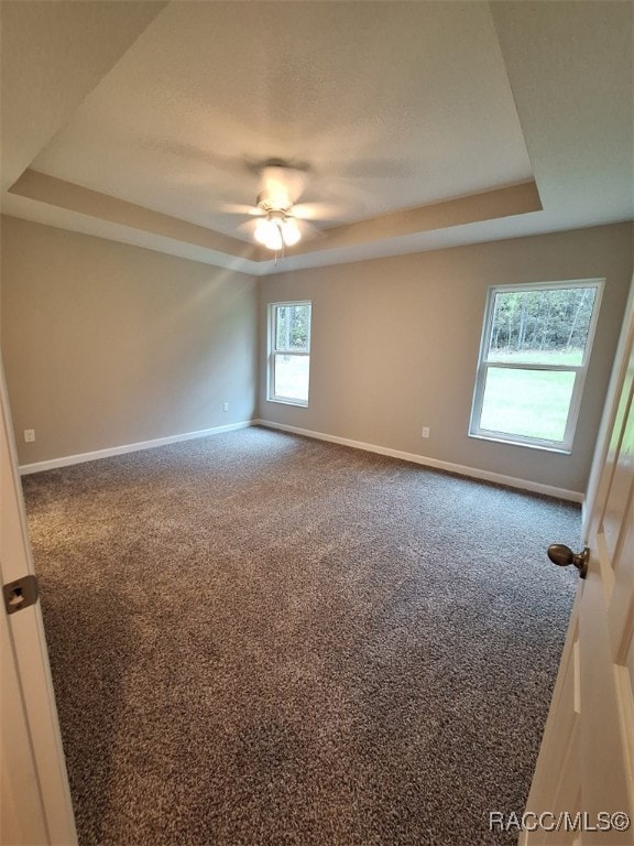 carpeted spare room with a raised ceiling and ceiling fan