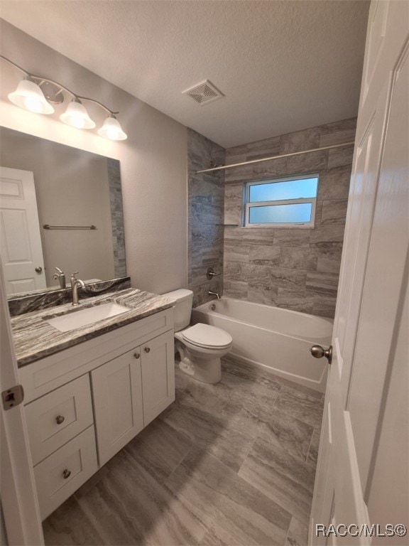 full bathroom with toilet, vanity, a textured ceiling, and tiled shower / bath