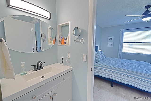 bathroom with hardwood / wood-style floors, vanity, ceiling fan, and a textured ceiling