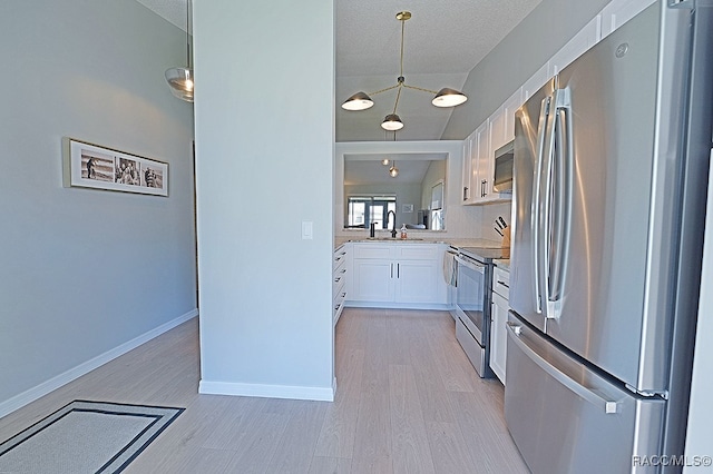 kitchen with white cabinets, appliances with stainless steel finishes, light hardwood / wood-style floors, and pendant lighting