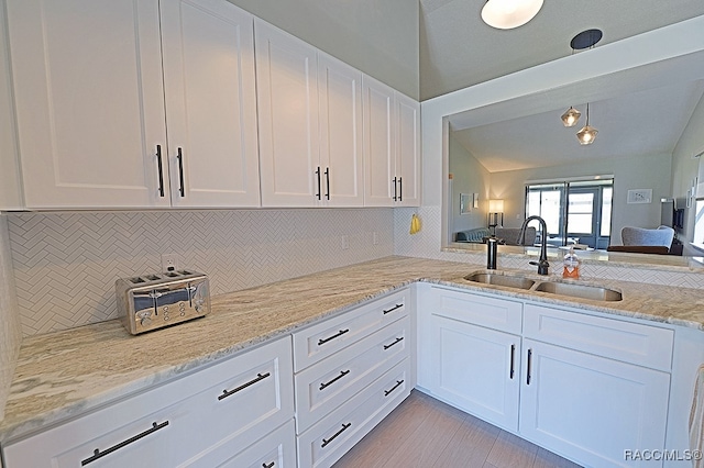 kitchen featuring light stone counters, white cabinetry, lofted ceiling, and sink