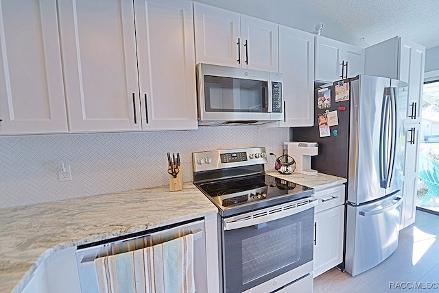 kitchen with white cabinetry, light stone counters, a textured ceiling, and appliances with stainless steel finishes