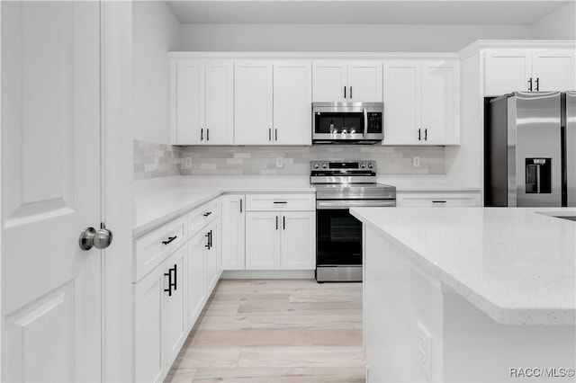 kitchen with white cabinets, decorative backsplash, stainless steel appliances, and light wood-style flooring