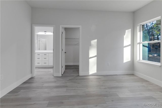 unfurnished bedroom featuring baseboards, a spacious closet, light wood-type flooring, ensuite bathroom, and a closet