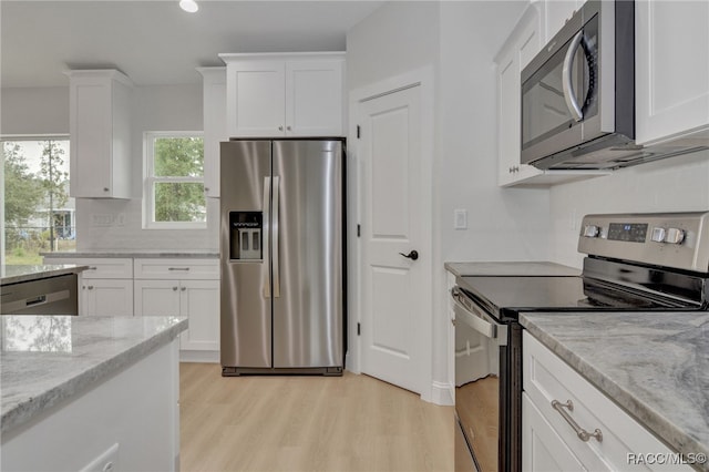 kitchen featuring light stone countertops, white cabinetry, stainless steel appliances, backsplash, and light wood-type flooring