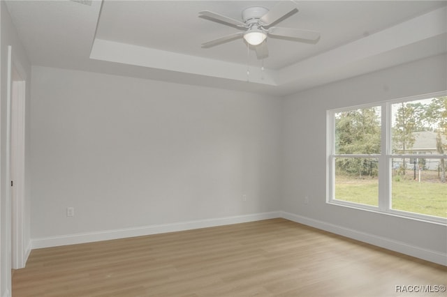 unfurnished room featuring ceiling fan, light hardwood / wood-style flooring, and a tray ceiling