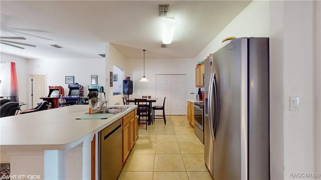 kitchen with stainless steel appliances, an island with sink, ceiling fan, decorative light fixtures, and light tile patterned flooring