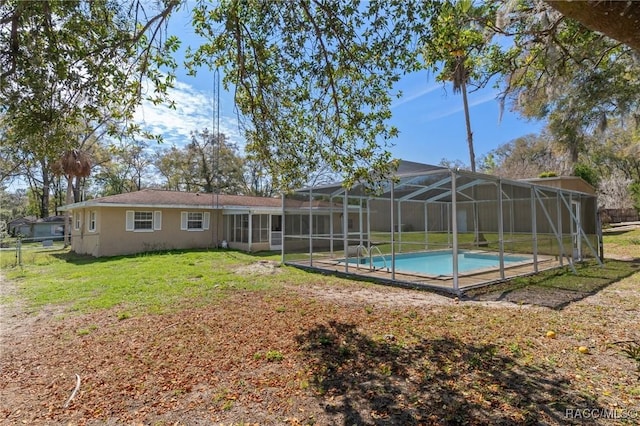 rear view of house with an outdoor pool, glass enclosure, a lawn, and stucco siding