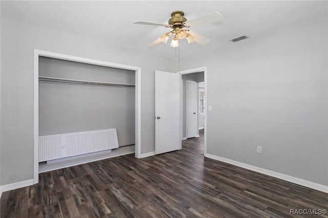 unfurnished bedroom with a closet, visible vents, radiator heating unit, wood finished floors, and baseboards