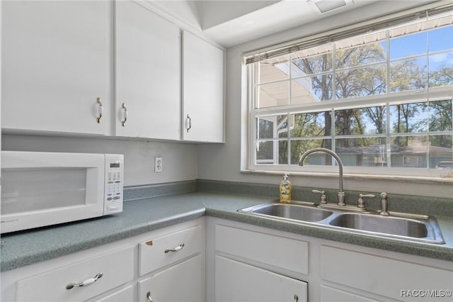 kitchen with white cabinetry, a sink, and white microwave