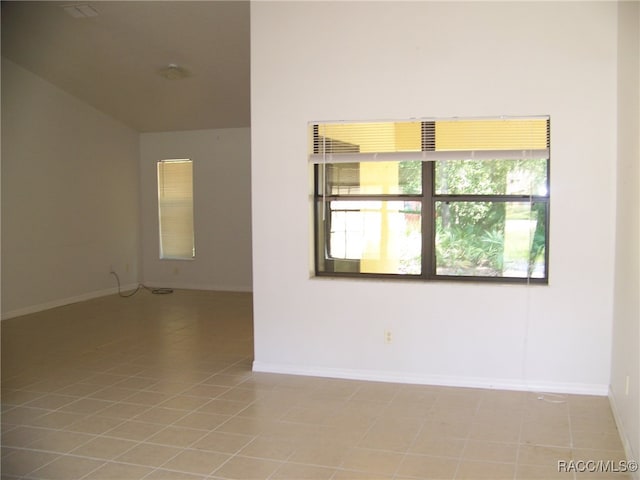 tiled spare room featuring lofted ceiling