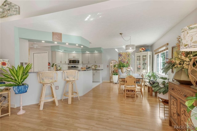 kitchen featuring a breakfast bar, light wood-type flooring, decorative backsplash, appliances with stainless steel finishes, and a peninsula