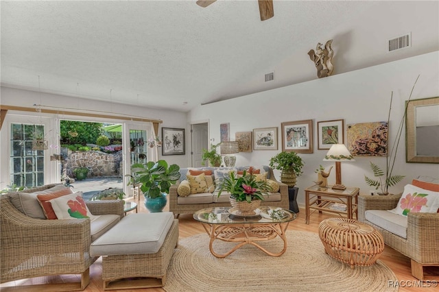 living room featuring lofted ceiling, wood finished floors, visible vents, and a textured ceiling