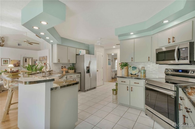 kitchen with a peninsula, a sink, appliances with stainless steel finishes, a kitchen breakfast bar, and backsplash