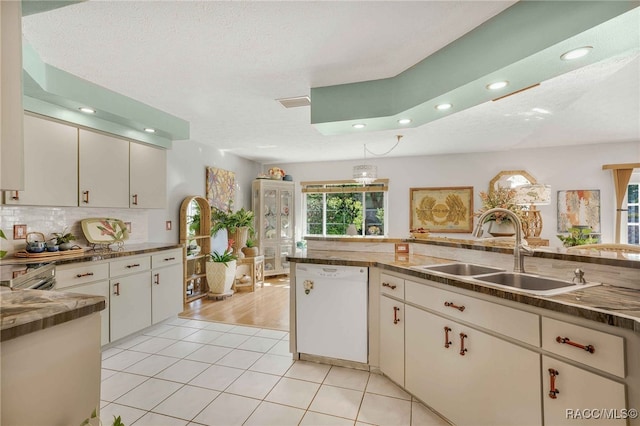 kitchen with a sink, tasteful backsplash, white cabinets, white dishwasher, and light tile patterned floors