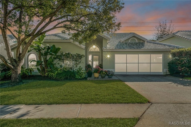 view of front of home featuring stucco siding, a lawn, a tile roof, concrete driveway, and an attached garage