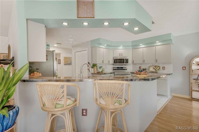 kitchen featuring a breakfast bar area, light wood finished floors, a peninsula, a sink, and appliances with stainless steel finishes