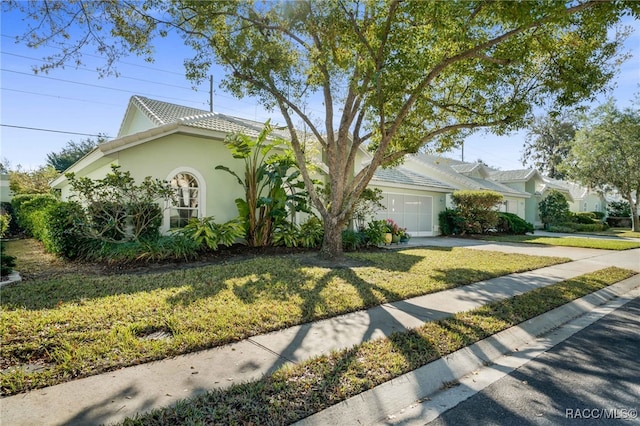 view of front of house with a tile roof, concrete driveway, a front yard, stucco siding, and an attached garage